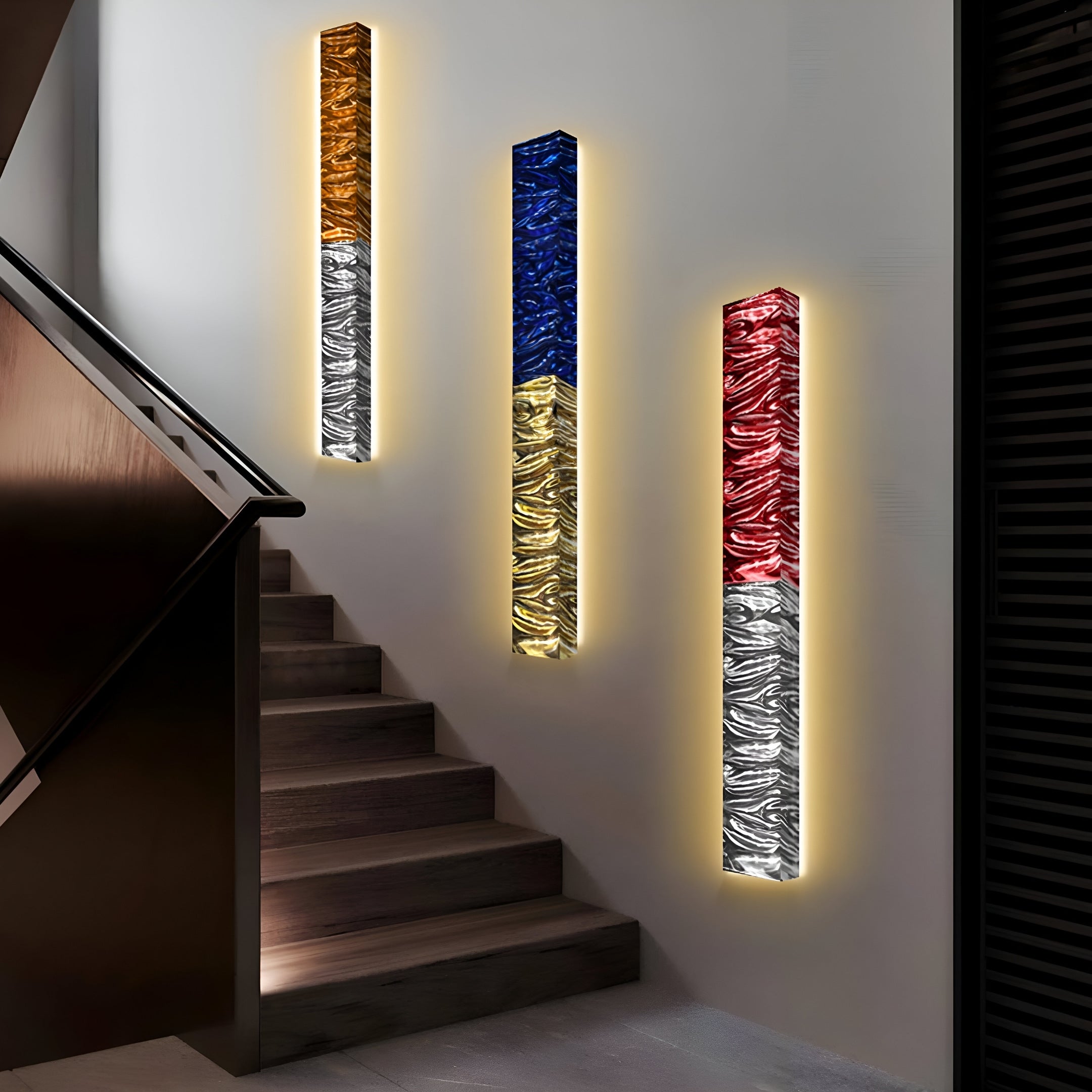 Giant Sculptures Textura 3D Red and Silver Leather Design Wall Art illuminates a staircase with abstract patterns of gold, blue, and red. This wall-mounted piece enhances the modern interior with its warm glow and stylish design elements.