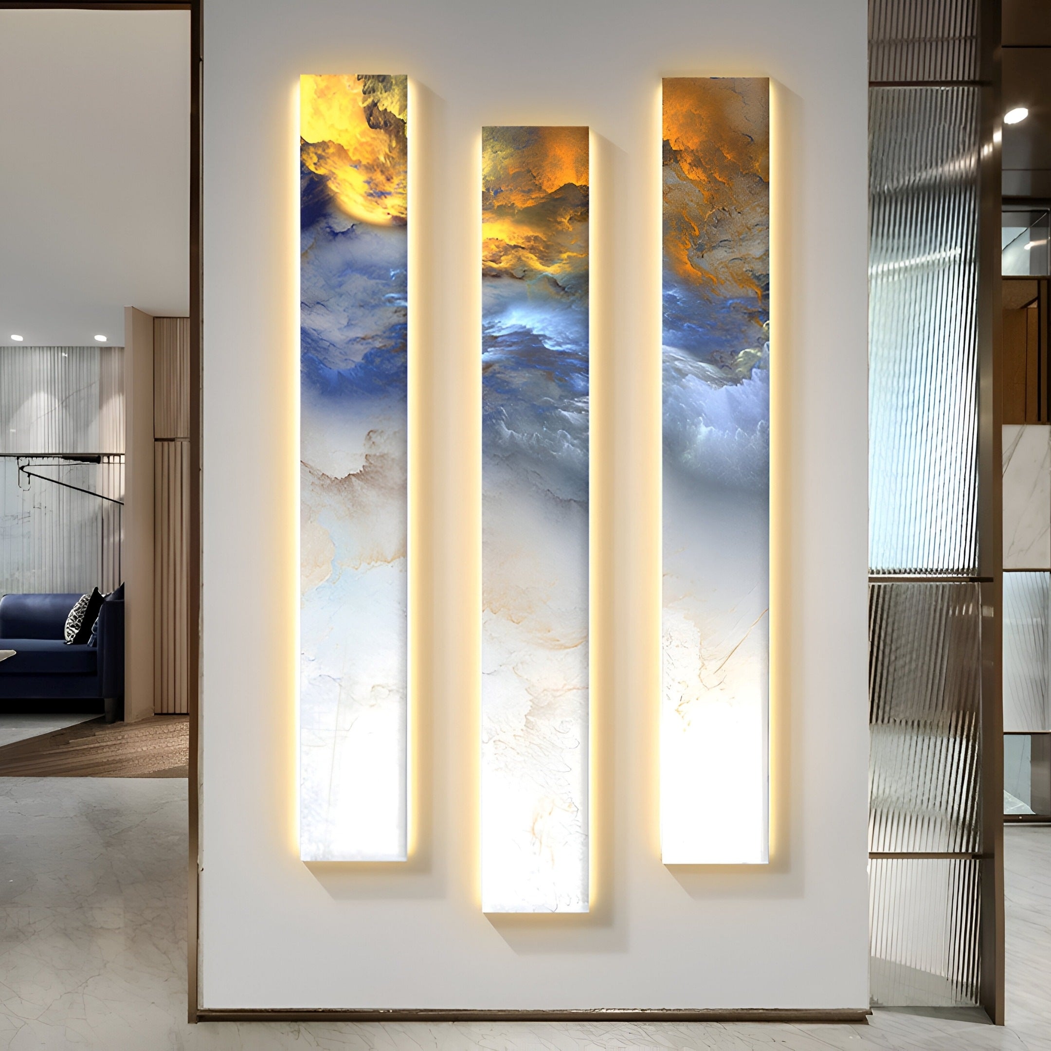 Experience the Chroma Sunset Fiery Strokes LED Wall Art by Giant Sculptures, showcasing three vertical panels in vibrant blue, orange, and white. Soft integrated lighting enhances its modern appeal within a visible living area.