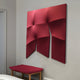 The Contours Deep Red Elastic Fabric 3D Wooden Wall Art by Giant Sculptures hangs above a wooden bench with a red cushion on a light gray wall, next to a doorway, in a minimalistic room.