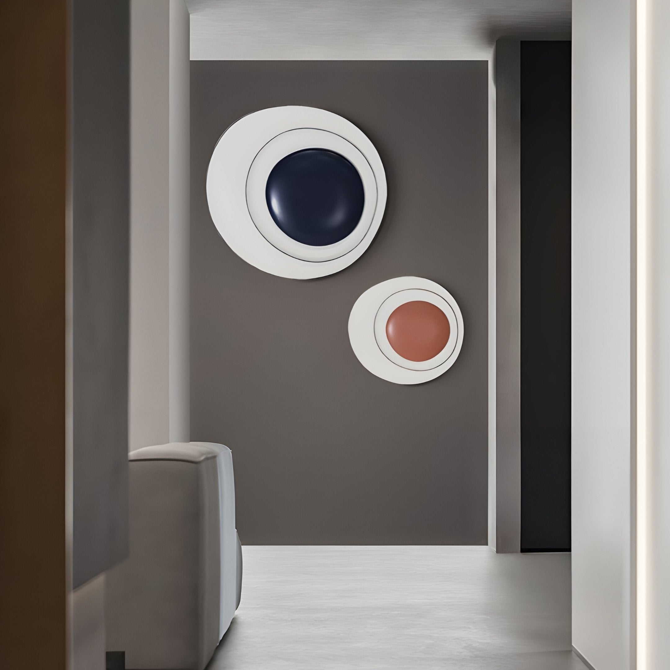 A modern room features a grey wall with Nordic-style 3D art by Giant Sculptures, including Aetherial Midnight Blue Glossy Circular Asymmetry with a midnight blue center and a smaller piece with a terracotta core. A light grey couch is partially visible on the left.