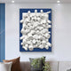 A Giant Sculptures Axion 3D wall art with a white wood cluster and sapphire blue edge adorns a light gray wall. Below it, a comfy beige and brown sofa with assorted cushions and a small plant adds warmth to the space.