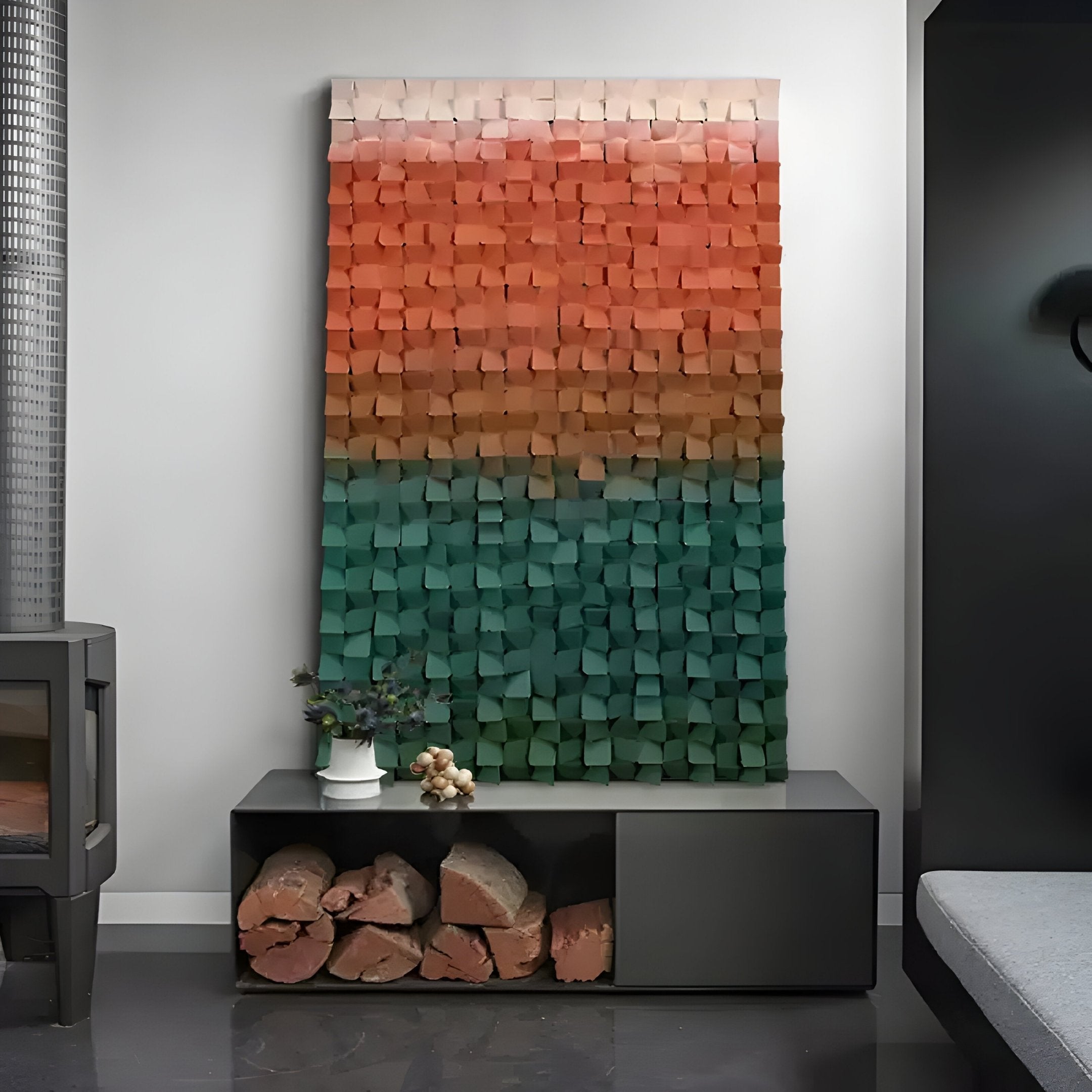 The white wall features the Stratiform Multitone Sunset Gradient Wood Mosaic 3D Wall Art by Giant Sculptures, with blocks transitioning from red to green. Below, a modern black shelf holds firewood and a small potted plant, while a fireplace sits cozily to the left.