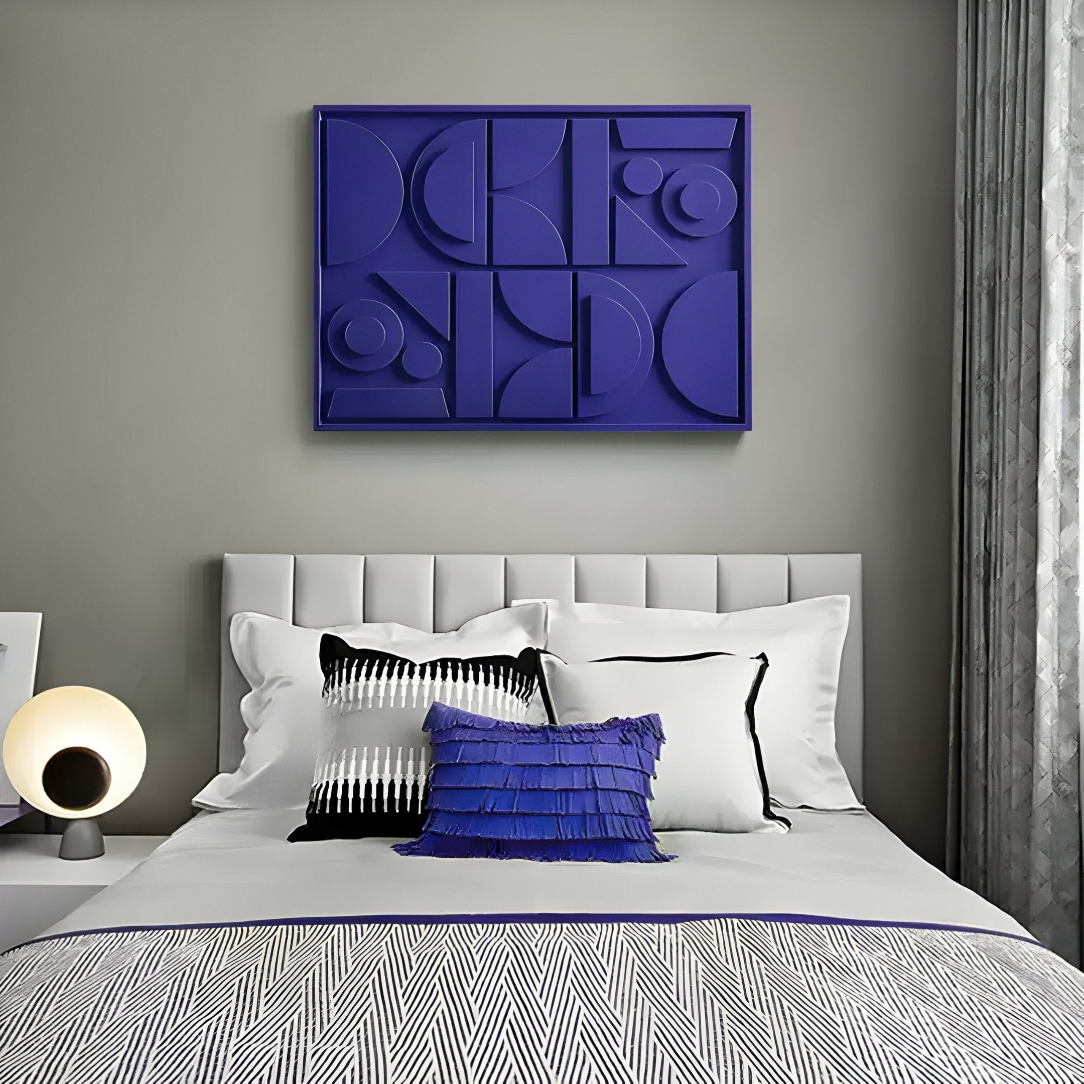 A modern bedroom features a white bed, geometric zigzag patterned throw, and blue accent pillows. A round lamp sits on the nightstand. Giant Sculptures Formate Royal Purple Geometric Wood Painted 3D Wall Art hangs on the gray wall, framed by gray and white curtains.