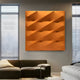 A modern living room features the Verto Vibrant Orange Stretch Fabric Layered Wooden 3D Wall Art by Giant Sculptures. To the left, a dark gray sofa with light cushions invites relaxation, while a bed is on the right. Two tall, narrow windows with blinds fill the space with natural light.