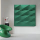 In a modern art installation by Giant Sculptures, the centerpiece is the Verto Emerald Green Stretch Fabric Layered Wooden 3D Wall Art. Below it, a sleek spiral chair sits tilted sideways, while to the left, a decorative column with a small white and red bust completes the contemporary scene.