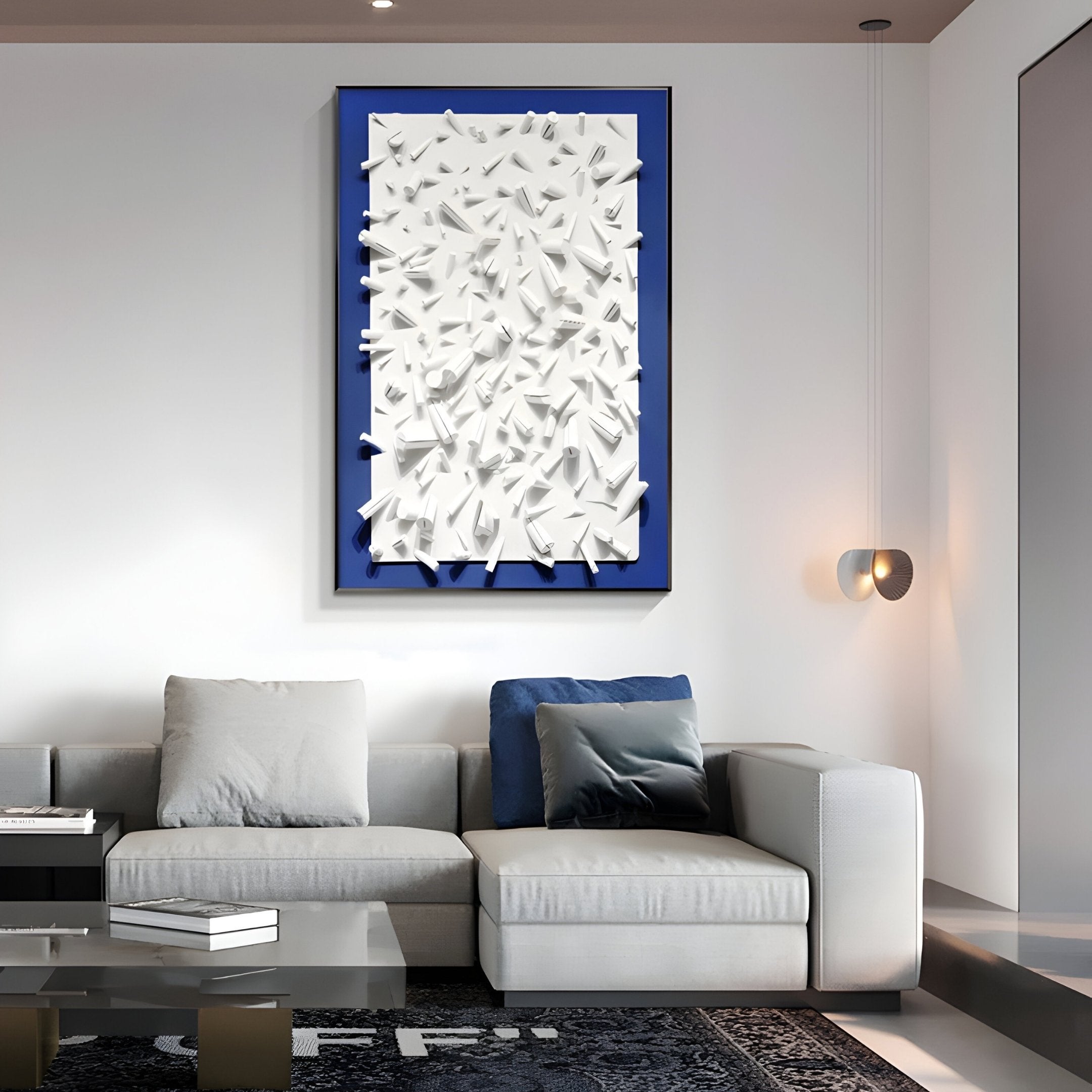 A modern living room includes a light gray sectional sofa with blue and gray cushions. Above, the Artiora Blue Edge & White Abstract Wooden Shard 3D Wall Art by Giant Sculptures displays white geometric shapes on a blue background. A small wall lamp provides a warm glow.