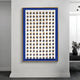 The Artiora Blue Edge & Wood Block Modular Grid 3D Wall Art by Giant Sculptures hangs on the wall, featuring a modular grid of cube-like shapes casting shadows for a striking pattern. It’s framed with a blue border and subtly includes a background plant.