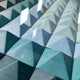 Close-up of the Viretta Teal Gradient Pyramid Textured 3D Wooden Wall Art by Giant Sculptures, featuring rows of pyramid-shaped tiles in varying blues and teals. The gradient casts shadows, enhancing the dimensions, ideal for modern living room decor.