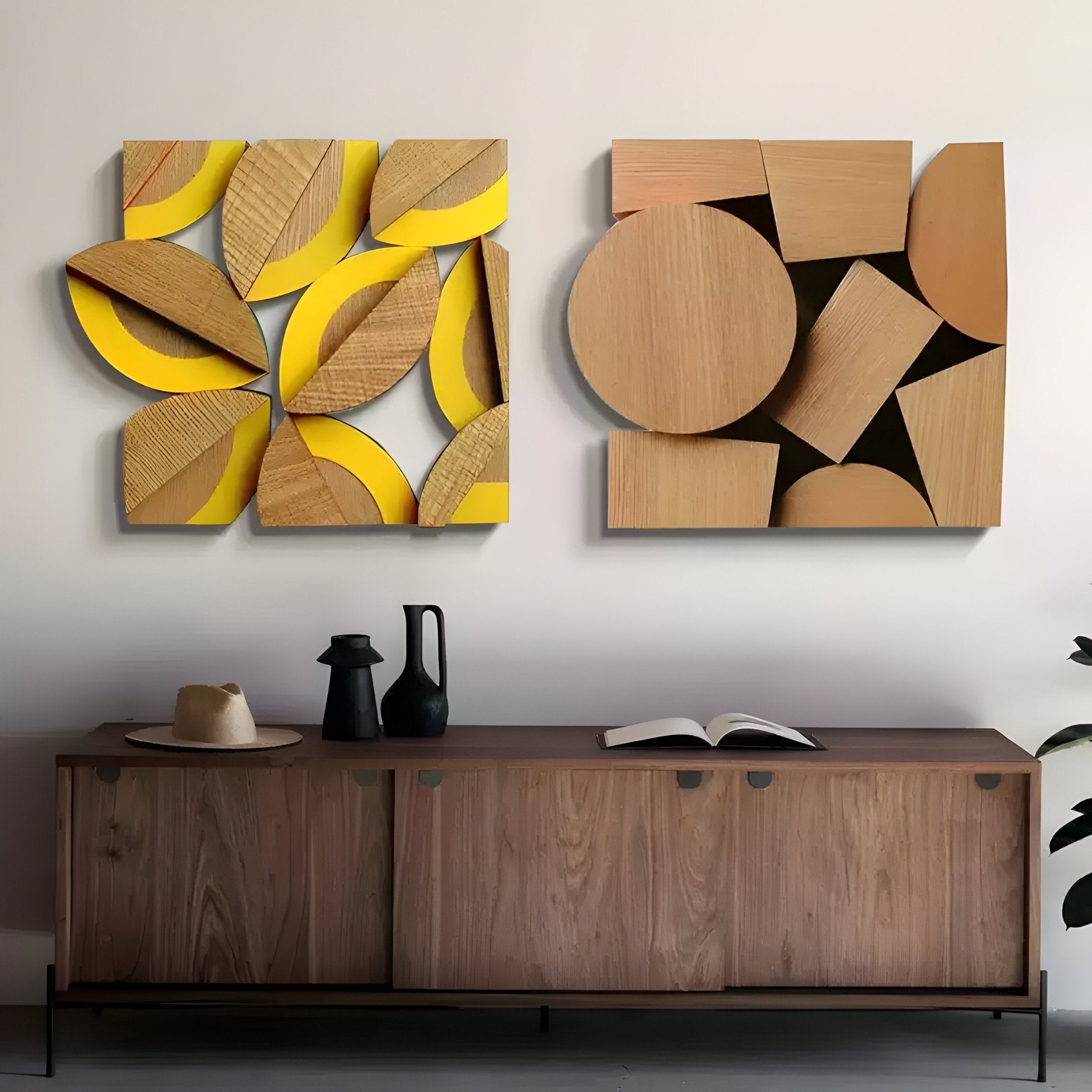 Against the wall stands a wooden sideboard topped with a hat, pitcher, and open book. Above it hang two Giant Sculptures Lignos 3D wall art pieces: one with circular cutouts over yellow, and another showcasing geometric shapes. A leafy plant peeks into view.