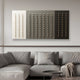 A minimalist living room with a gray sectional and neutral-toned throw blanket. The Contrasto Monochrome Symmetry 3D Wooden Wall Art by Giant Sculptures, featuring small pegs on beige, gray, and black panels, hangs above the sofa. A round coffee table sits in the foreground.