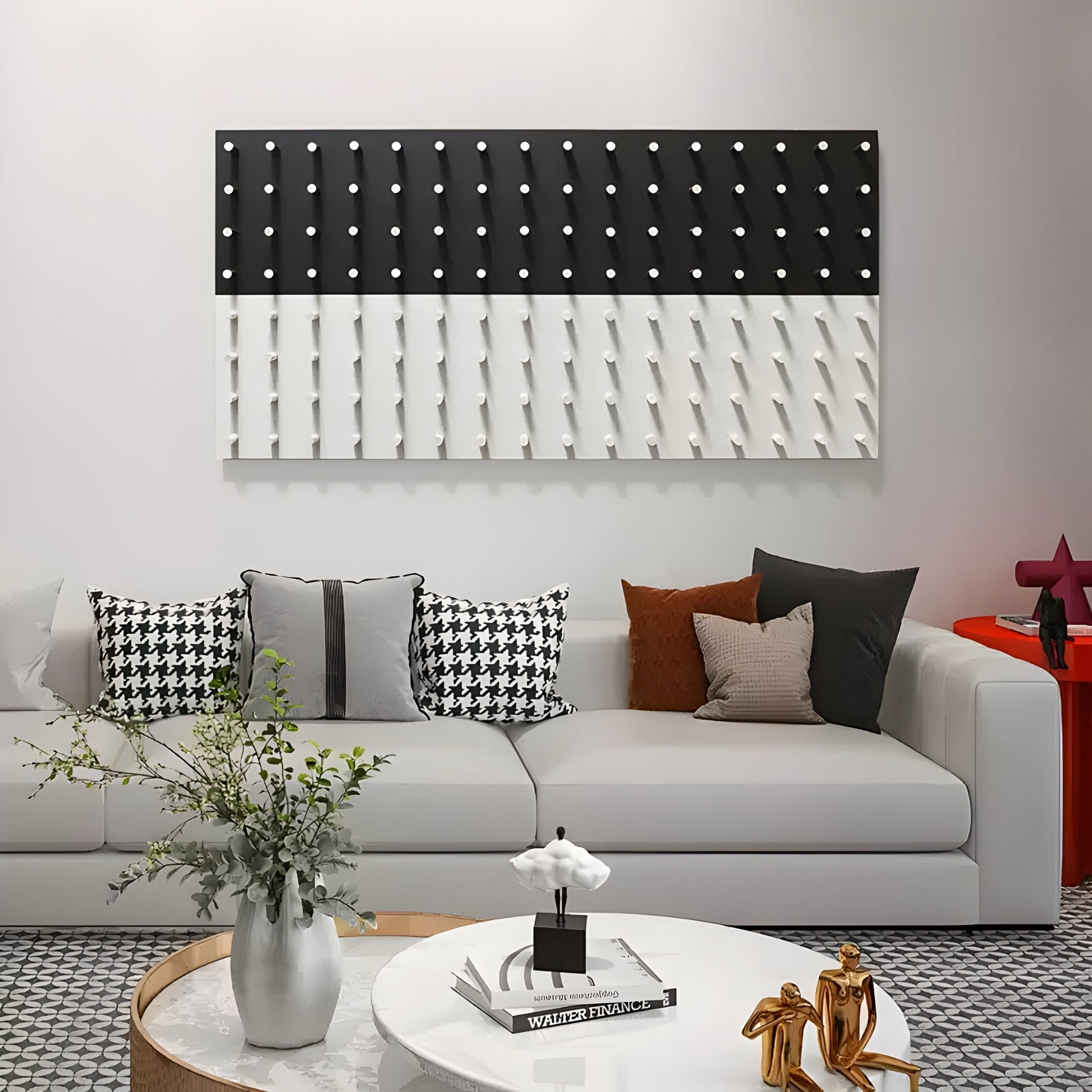 A modern living room exuding elegance features a white sofa adorned with houndstooth and solid cushions. Beside the circular table holding a plant and magazines, Giant Sculptures Contrasto Black & White Linear 3D Wooden Wall Art graces the wall, adding depth to the serene space.