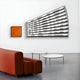 The modern interior showcases a red curved sofa, two round white tables, and the BOOM 3D wooden wall art by Giant Sculptures displaying white text on gray stripes. A vibrant orange square artwork adds contrast, perfectly enhancing the rooms dynamic style.