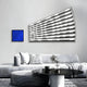 Modern living room featuring a sleek gray sofa, monochrome pillows, and a round black coffee table. Abstract wall art with blue and black geometric shapes pairs with the Illustra Deep Blue Highlight BOOM Text 3D Wooden Wall Art by Giant Sculptures showcasing a dynamic striped design.