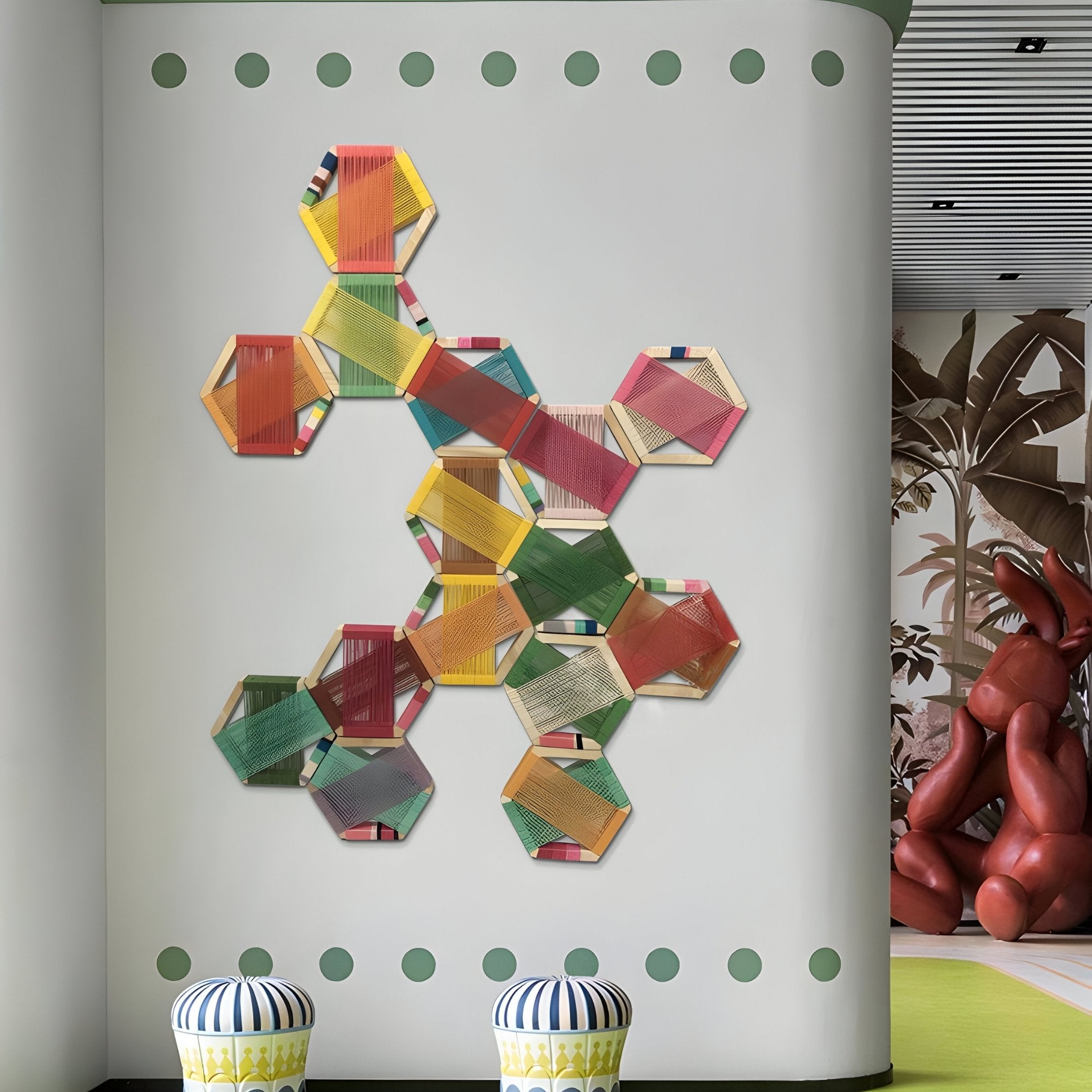 A Spectra III Multicoloured Interwoven Hexagonal Frame 3D Wall Art by Giant Sculptures is displayed on a white wall dotted with green. In front sit two striped dome stools, while abstract art and curved architecture enhance the scene with striking geometric precision.