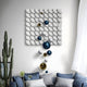 Modern living room with Giant Sculptures Orbina White 3D Wood Relief Wall Art featuring blue & gold metal balls. A tall cactus in the corner complements the sofa with blue cushions under a window with sheer curtains, enhancing the modern aesthetic.