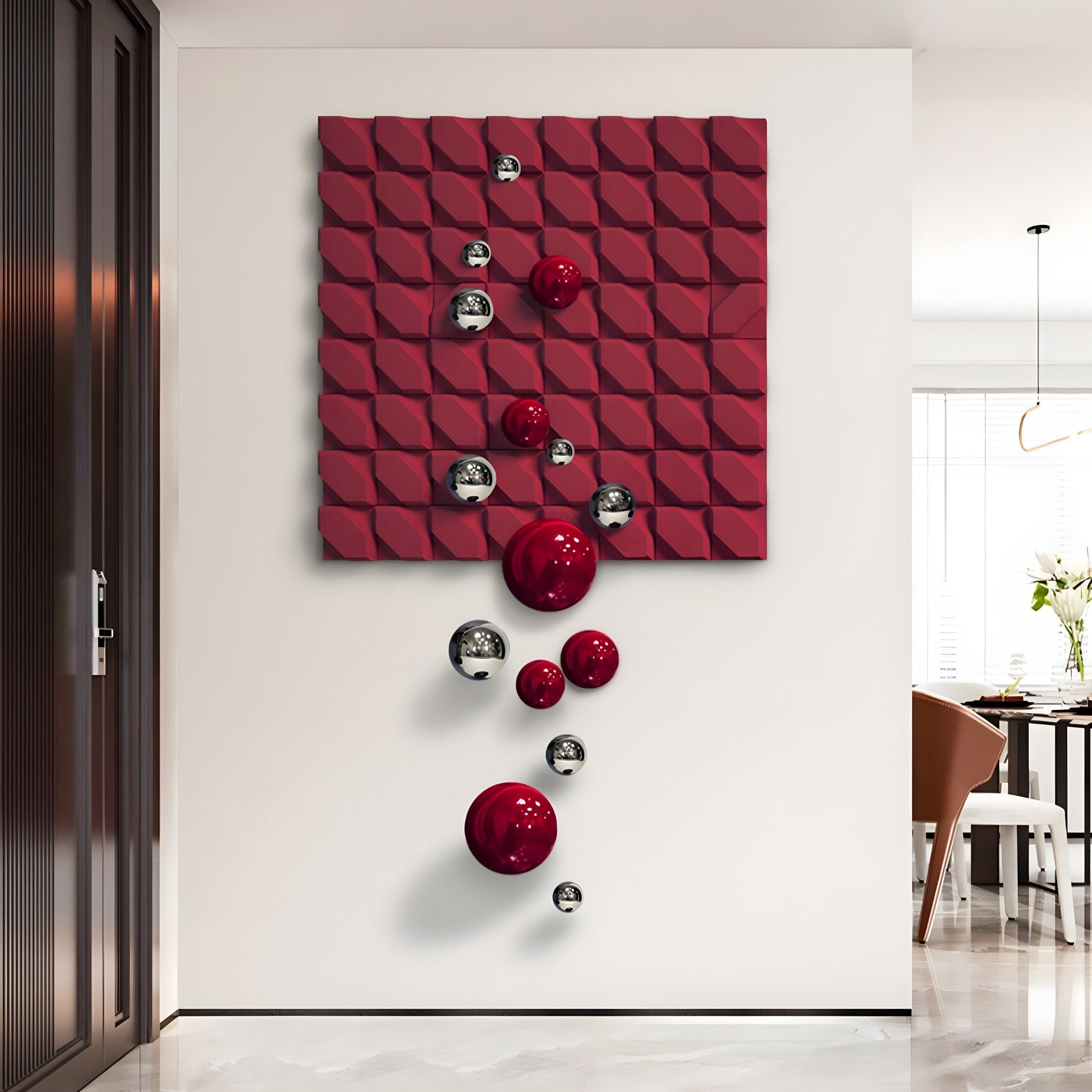 A modern art installation on a white wall features the Orbina Crimson Red 3D Wood Relief Wall Art With Metal Ball by Giant Sculptures. It showcases geometric patterns with shiny red and silver spheres cascading down, creating a striking visual effect. A dining area is visible to the right.