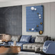 A modern living room features a grey and blue sectional sofa and an Orbison Sky Blue 3D Wood Relief Wall Art With Metal Ball by Giant Sculptures. A coffee table with decorative objects complements the sleek, contemporary design.