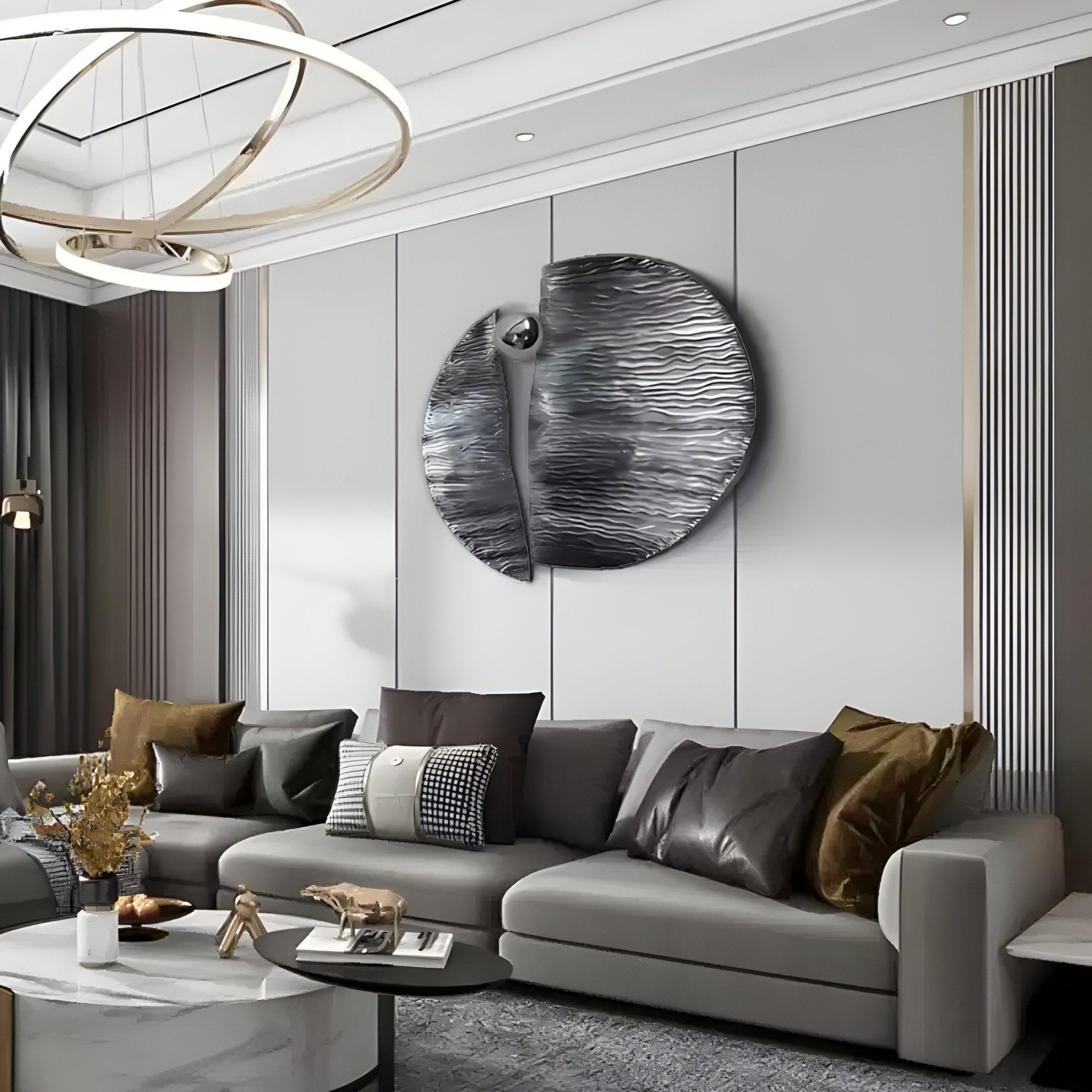 A modern living room features a spacious gray sectional with pillows and is highlighted by the Argentum Textured Wood Relief 3D Wall Art With Silver Metal Ball by Giant Sculptures on the gray wall. A round coffee table below a contemporary chandelier completes the neutral-toned setting.