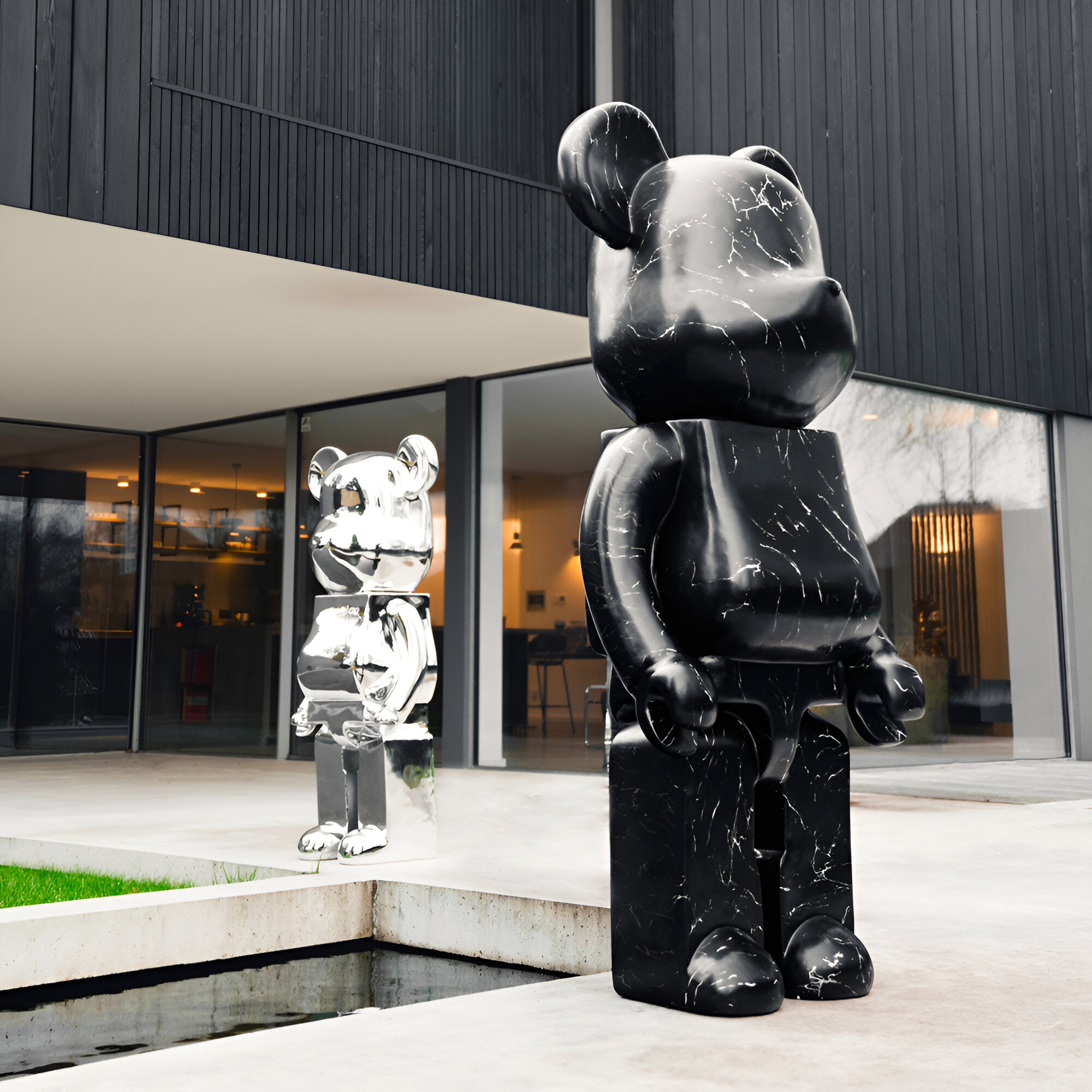 Two large bear sculptures in a modern setting. The larger bear is black with a marble-like texture, while the smaller bear is silver and reflective. Contemporary outdoor decor for luxury spaces.