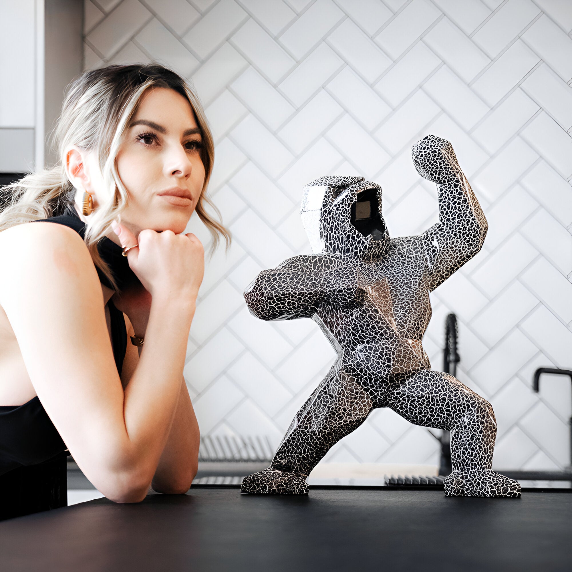 Lifestyle photo of a black and white cracked Gorilla sculpture next to a woman in a modern kitchen setting. The Gorilla sculpture exudes contemporary art and luxury decor, blending seamlessly into the minimalist interior design.