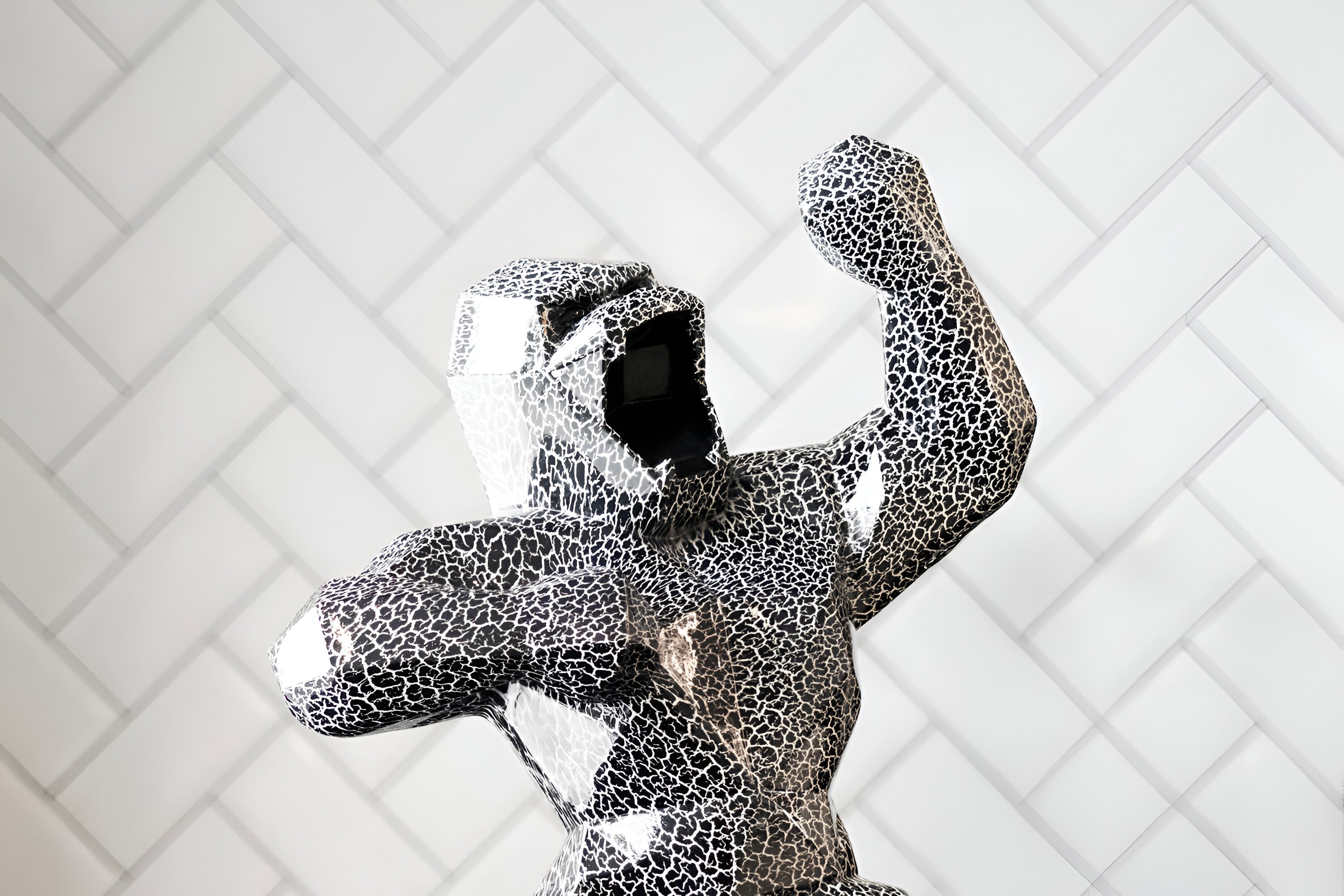 White and black crackled design on a geometric gorilla sculpture with a glossy finish, set against a background of white herringbone tiles.